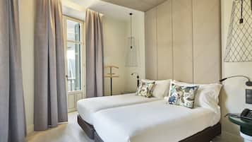 Een moderne hotelkamer met twee bedden, een groot raam met gordijnen, een hanglamp en een aan de muur bevestigd telefoon.