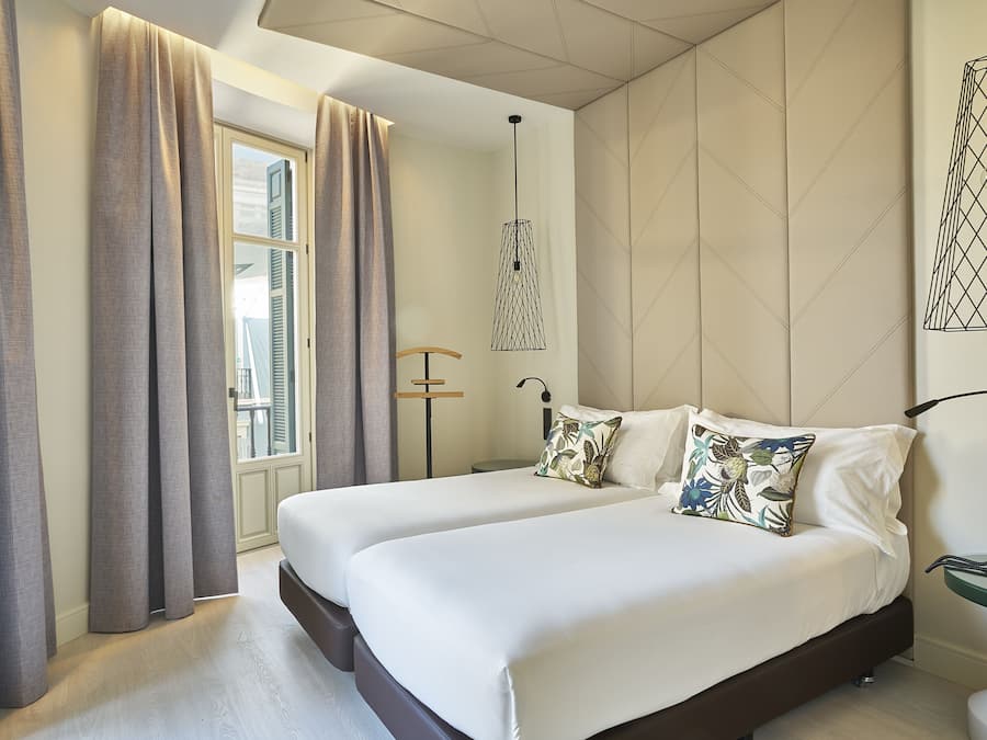 Een moderne hotelkamer met twee bedden, een groot raam met gordijnen, een hanglamp en een aan de muur bevestigd telefoon.