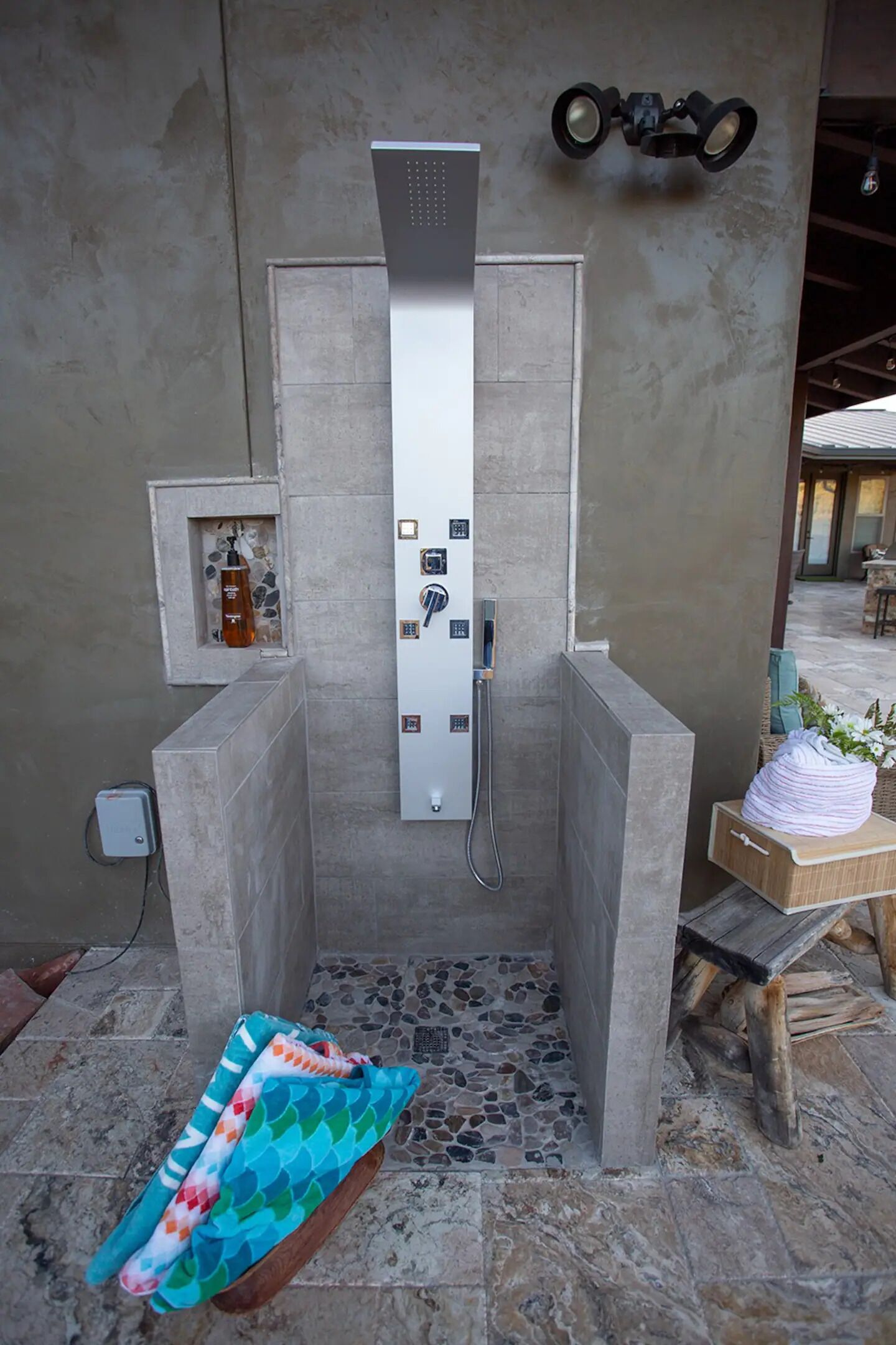 A modern shower enclosure with a control panel, a small shelf with toiletries, and a wooden bench with a towel.
