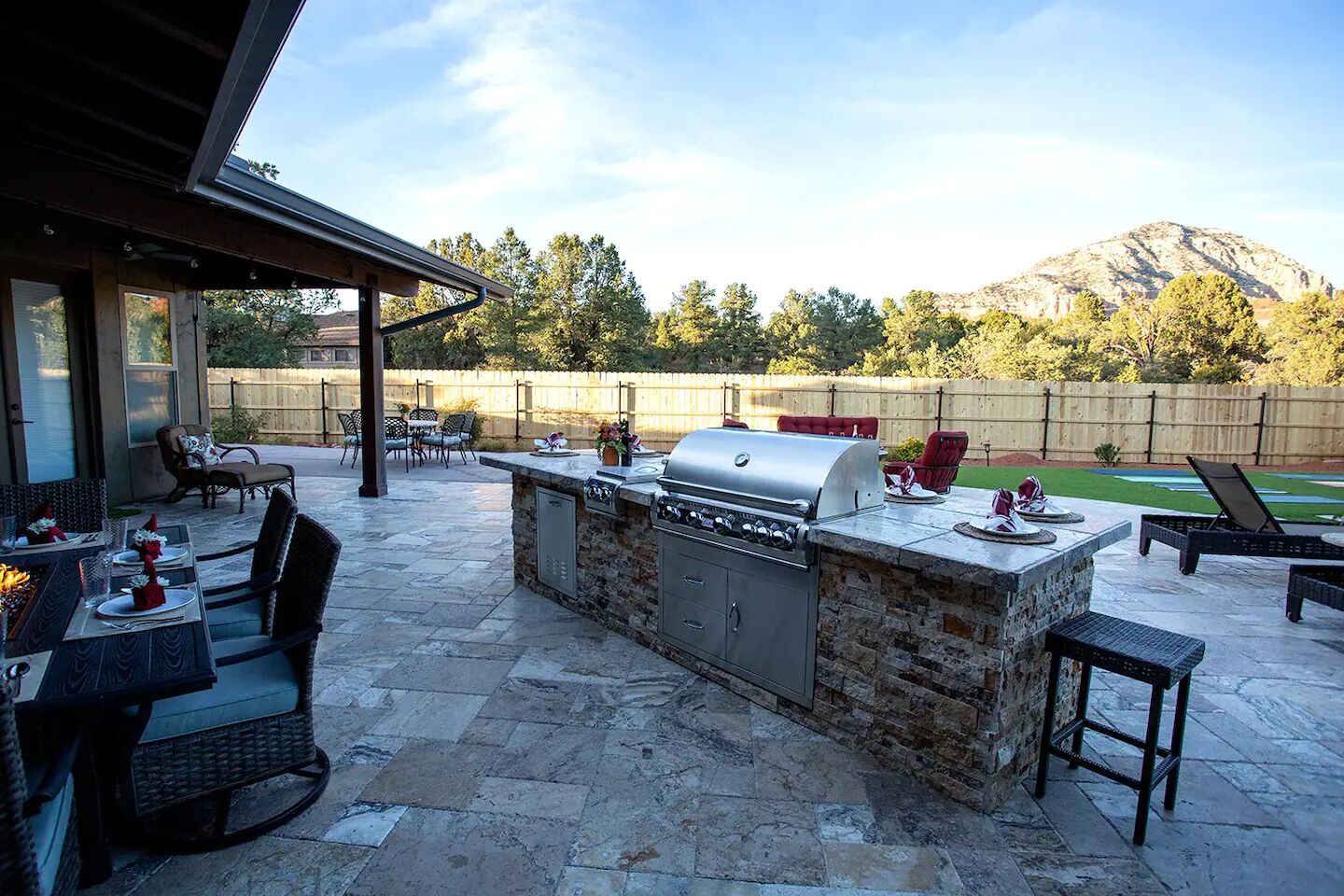Een terras buiten met een barbecue van natuursteen, een zithoek en uitzicht op een berg.