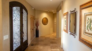 Un pasillo con piso a cuadros, una puerta de vidrio con diseño decorativo y obras de arte enmarcadas en las paredes.