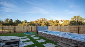 Un patio trasero con un jacuzzi, escalones de piedra y una valla de madera.
