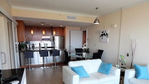 Una sala de estar moderna con un sofá blanco, una mesa de centro de vidrio y un comedor con una mesa y sillas blancas.