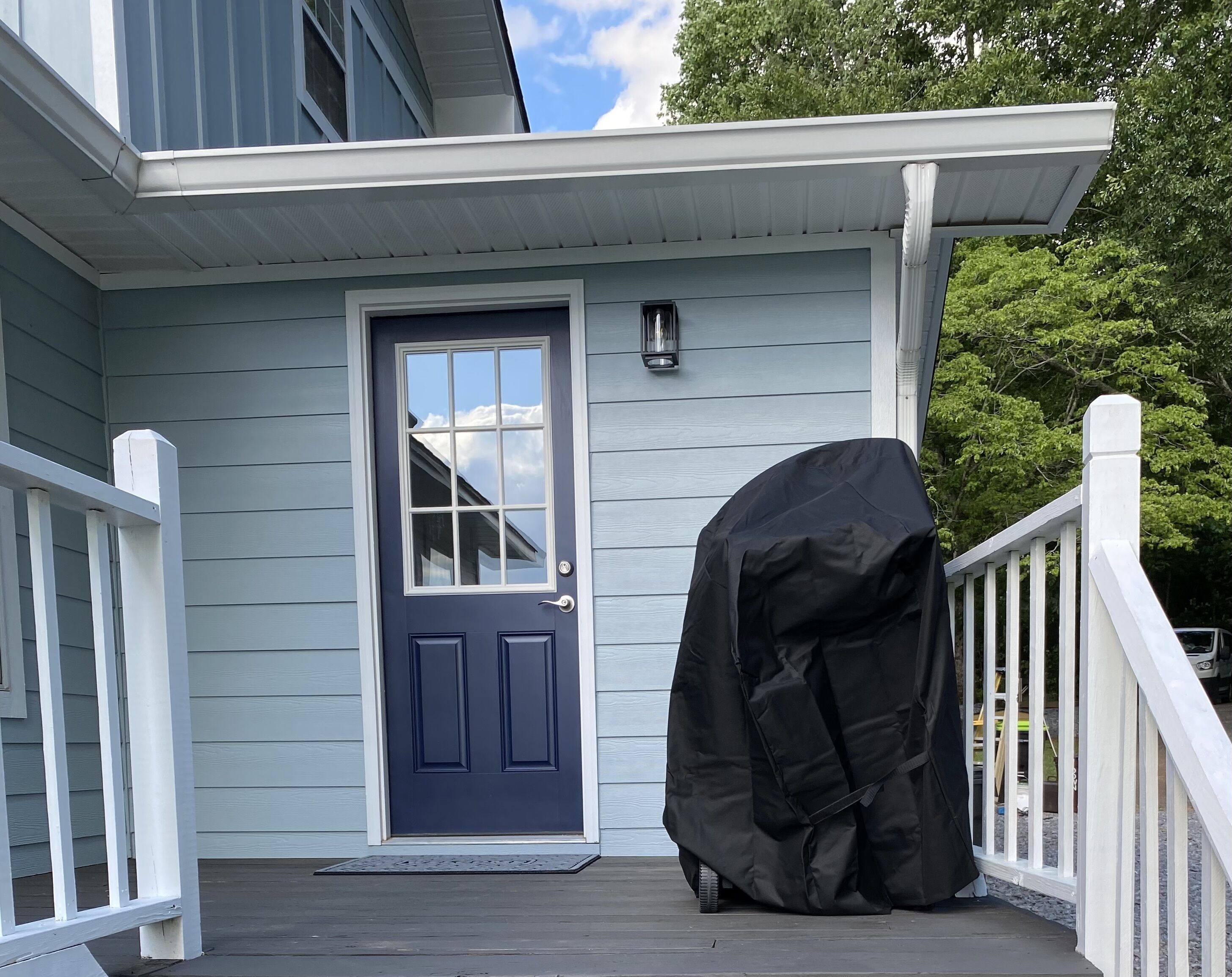 A house with a dark blue front door, a covered grill, and a white porch railing.