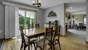 A dining area with a wooden table and chairs, a chandelier, and a view of the outdoors through large sliding glass doors. - Charming Modern Victorian in the Village of EVL (Ellicottville)