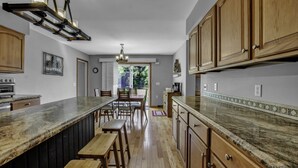 A kitchen with wooden cabinets, a granite countertop, and a dining area with chairs and a bench. - Charming Modern Victorian in the Village of EVL (Ellicottville)