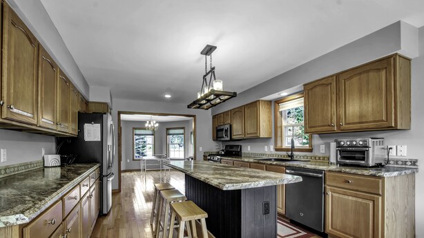 A spacious kitchen with wooden cabinets, a central island with stools, and modern appliances. - Charming Modern Victorian in the Village of EVL (Ellicottville)