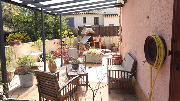 En täckt uteplats med trädgårdsmöbler, krukväxter och en tegelugn.