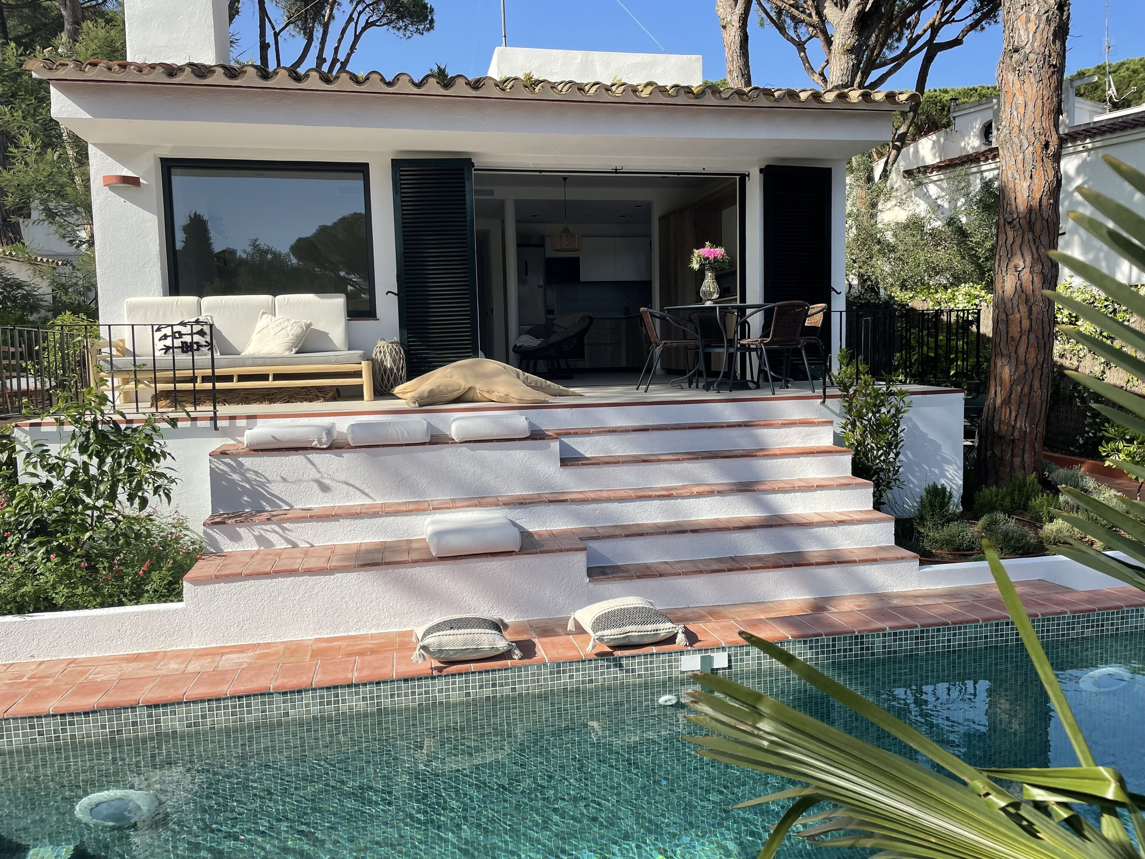 Una casa moderna con piscina, escalones que llevan a un patio y mobiliario de exterior.