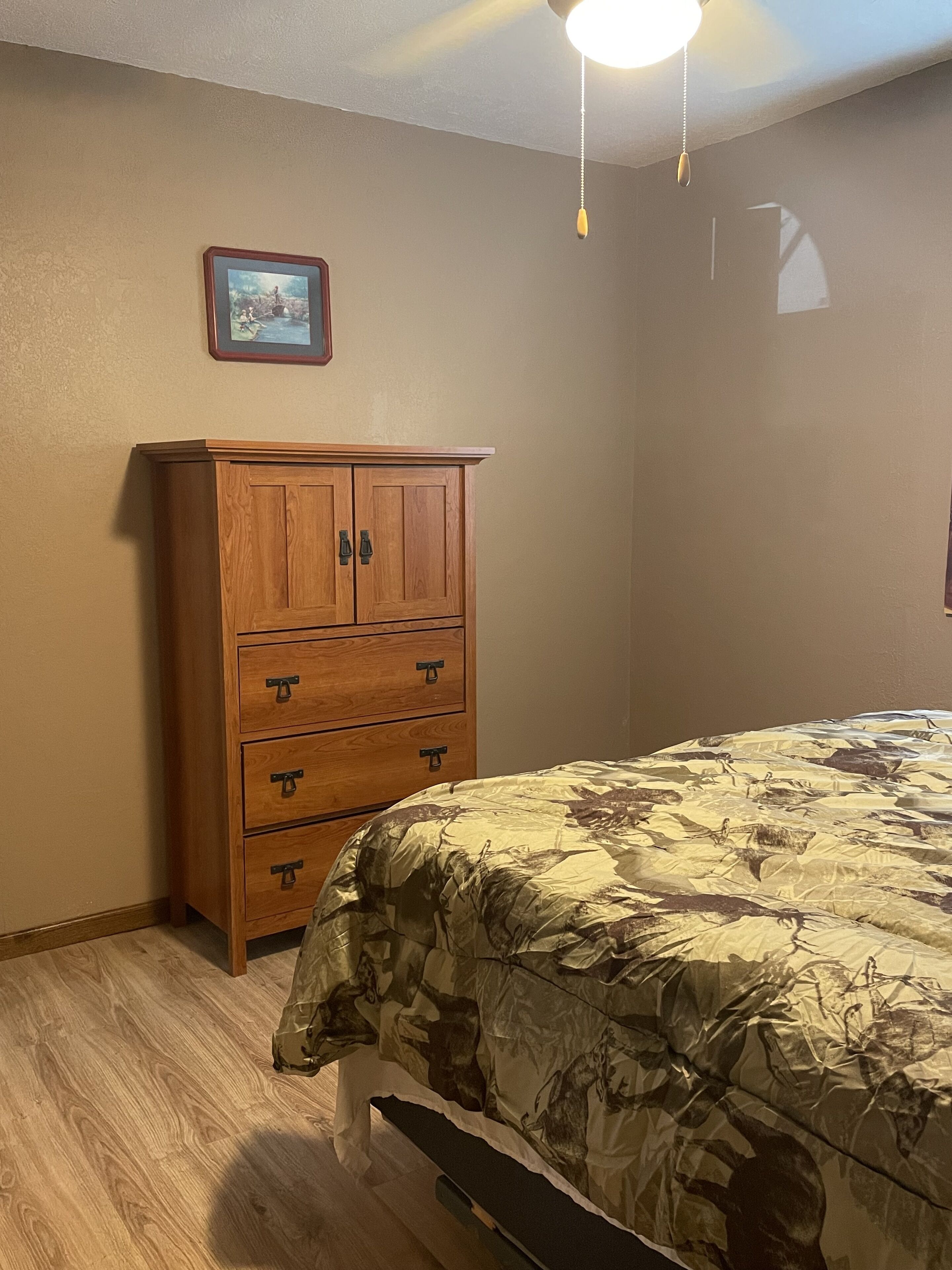 Ein Schlafzimmer mit einem Holzkleiderschrank, einem Bett mit Tarnmuster-Bettdecke und einem Deckenventilator.