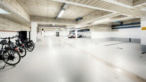 Ett rent och väl upplyst parkeringsgarage med vita väggar och ett kaklat tak. Flera cyklar står parkerade på vänster sida, och en bil syns på avstånd.