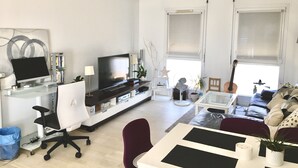 En moderne stue med et fladskærms-tv, et glasbord, en hvid sofa og en rød lænestol.