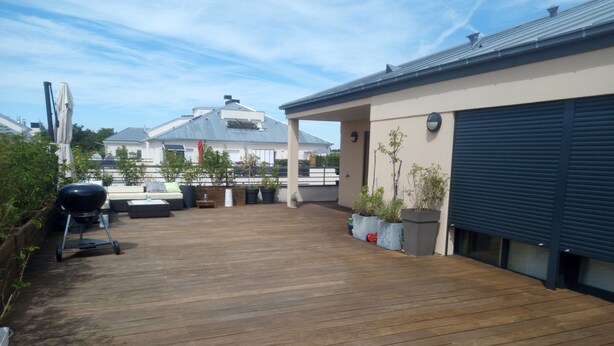 En træterrasse med grill, udendørs møbler og plantekasser.