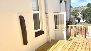 A wooden deck with a white building featuring a satellite dish, a window, and a door. - Retreat 3 bedroomed apartment (Stonehouse)