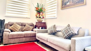 A living room with two sofas, a red rug, a floral centerpiece, and a painting on the wall. - Retreat 3 bedroomed apartment (Stonehouse)