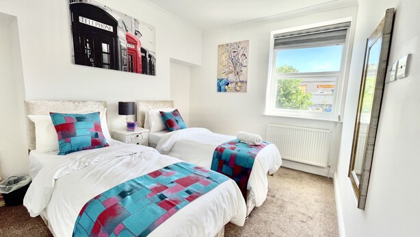 A hotel room with two beds, a large window with a view, a telephone art piece on the wall, and a radiator. - Retreat 3 bedroomed apartment (Stonehouse)