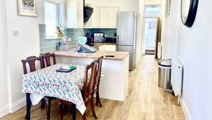 A modern kitchen with a central island, wooden dining table, and a view to the living area. - Retreat 3 bedroomed apartment (Stonehouse)