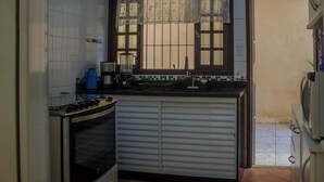 A compact kitchen with a stove, oven, and a window with lace curtains. - Piscina Aquecida, Ar Condicionado, Área Gourmet, Bilhar (Itanhaém)