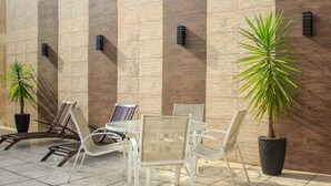 Outdoor seating with chairs and tables, potted plants, and a textured wall with vertical lines. - Piscina Aquecida, Ar Condicionado, Área Gourmet, Bilhar (Itanhaém)