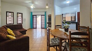 A living room with a sofa, a dining table with chairs, a ceiling fan, and a kitchen area visible through an open door. - Piscina Aquecida, Ar Condicionado, Área Gourmet, Bilhar (Itanhaém)