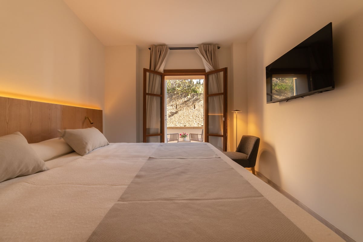Een hotelkamer met een bed, een aan de muur bevestigde televisie en uitzicht op het omliggende landschap.