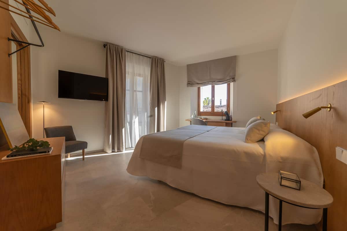 Hotelkamer met een groot bed, een bureau, een stoel, een aan de muur bevestigde televisie en een raam met gordijnen.