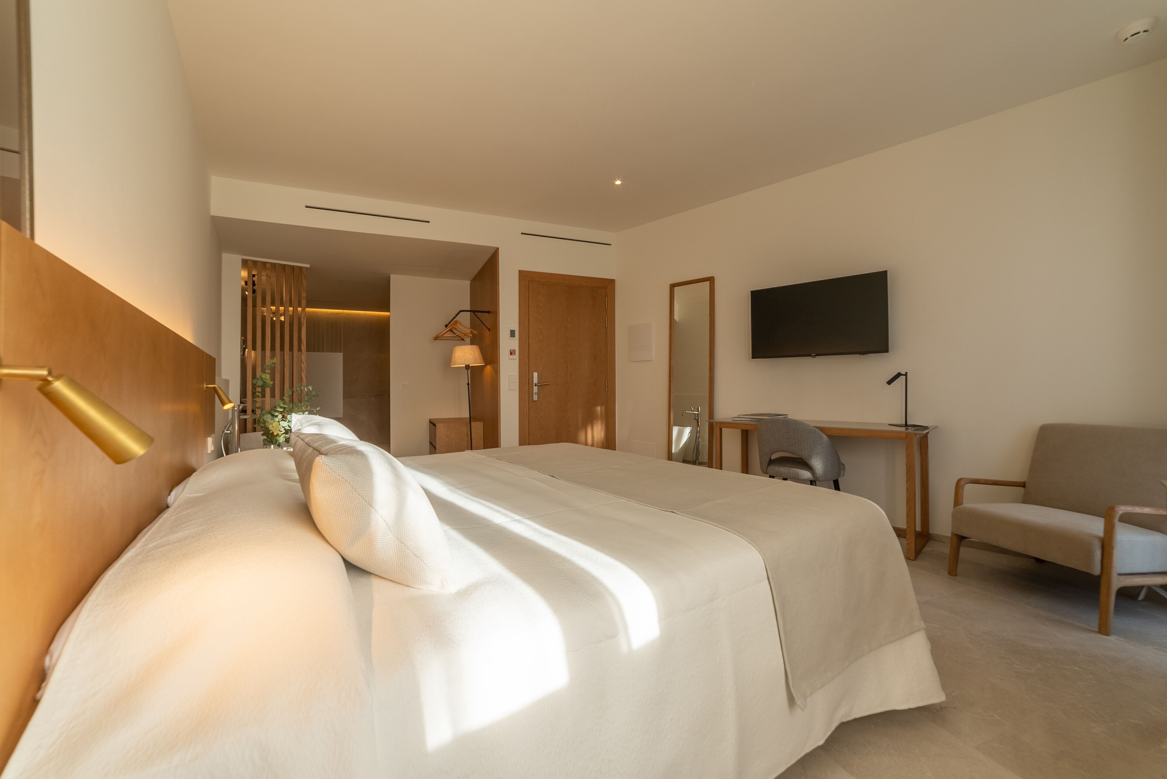 Una habitación de hotel moderna con una cama grande, un escritorio, una silla y un televisor montado en la pared.