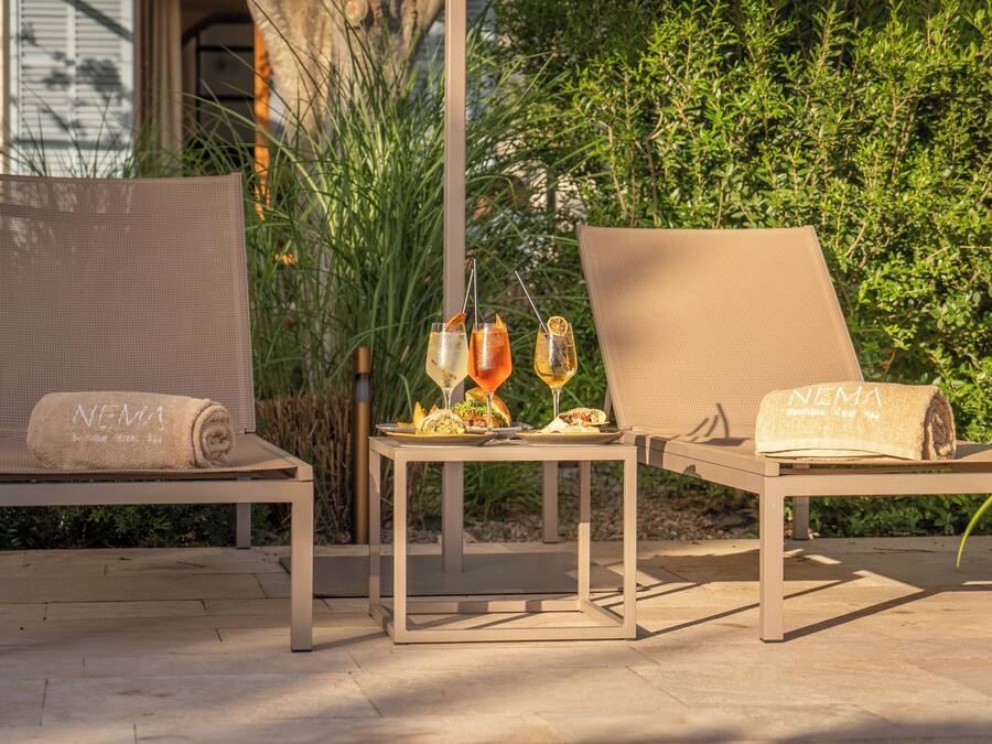 Dos sillones de descanso con toallas, una mesa con bebidas y un fondo de follaje.