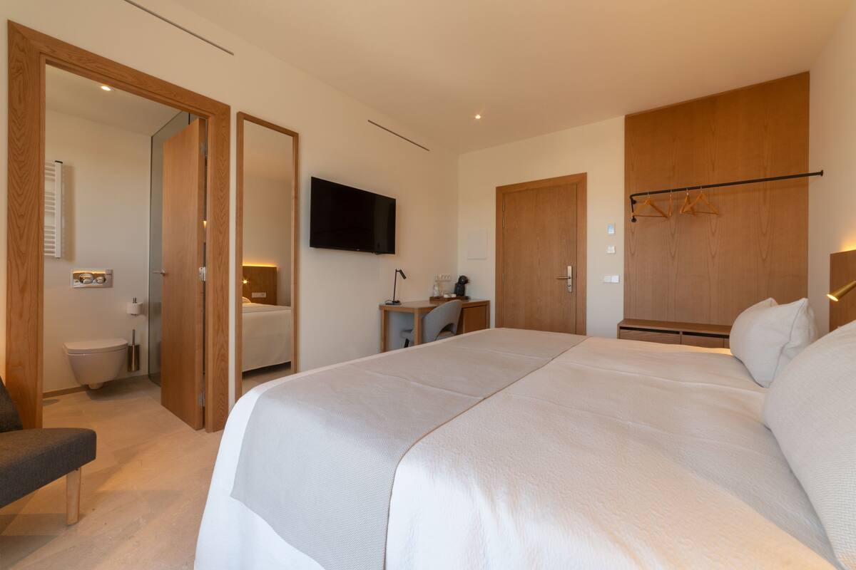 Een slaapkamer met een groot bed, een bureau met stoel, een televisie en een kledingkast.