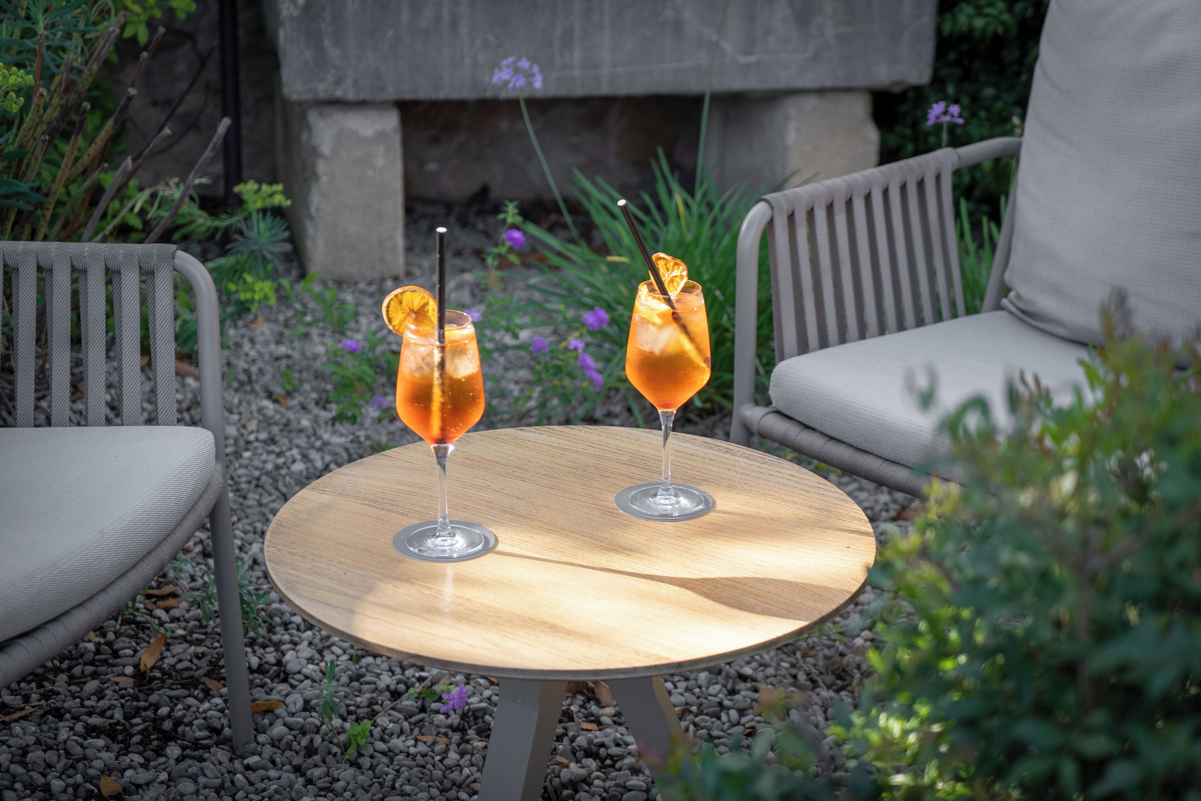 Two drinks on a round wooden table with chairs around it.