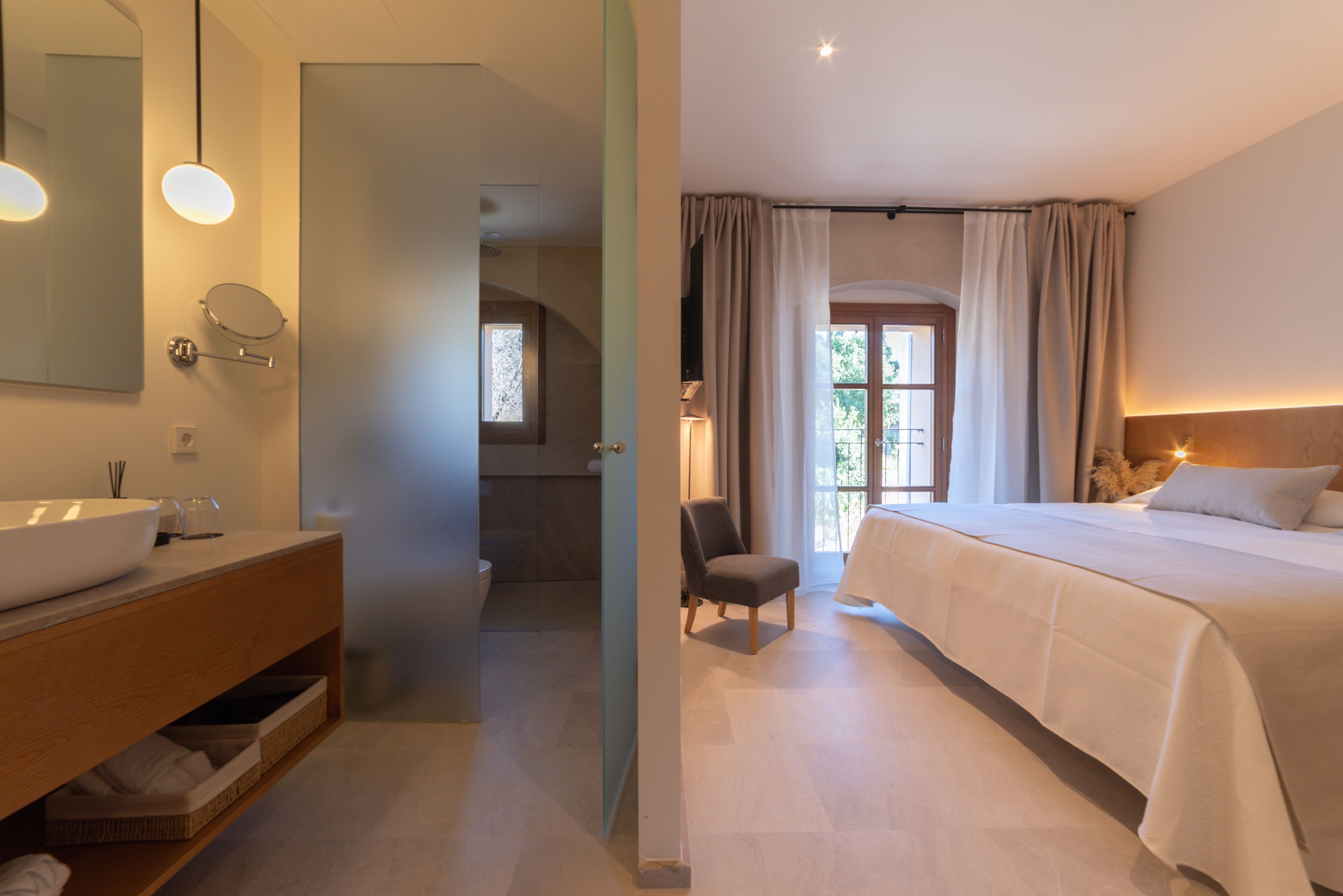 A hotel room with a large bed, a bathroom with a sink and mirror, and a view of the outdoors through a window.