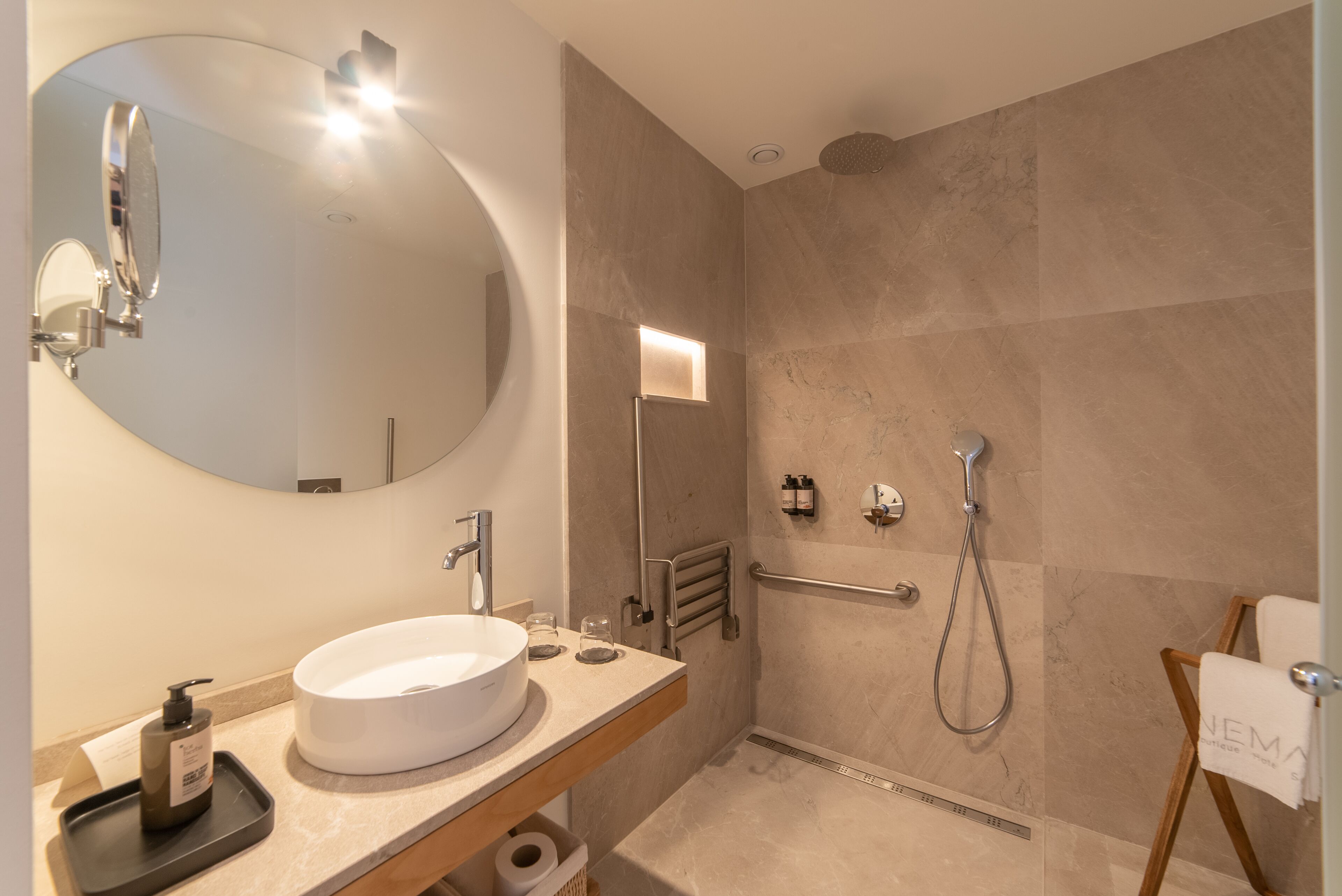 Un baño moderno con un espejo redondo, un lavamanos, un cabezal de ducha de mano y un perchero para toallas.