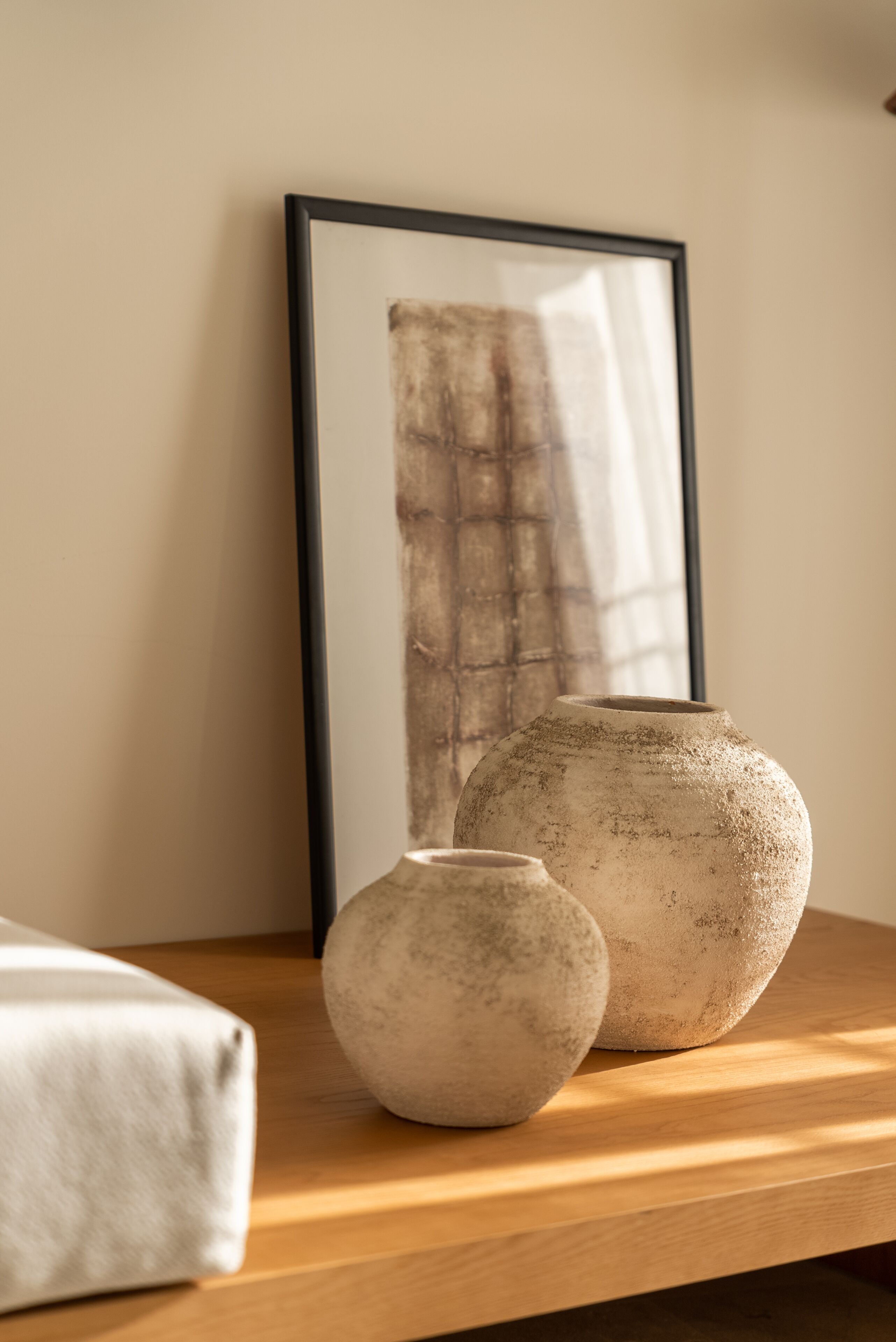 Una mesa de madera con dos jarrones de cerámica y un cuadro abstracto enmarcado.