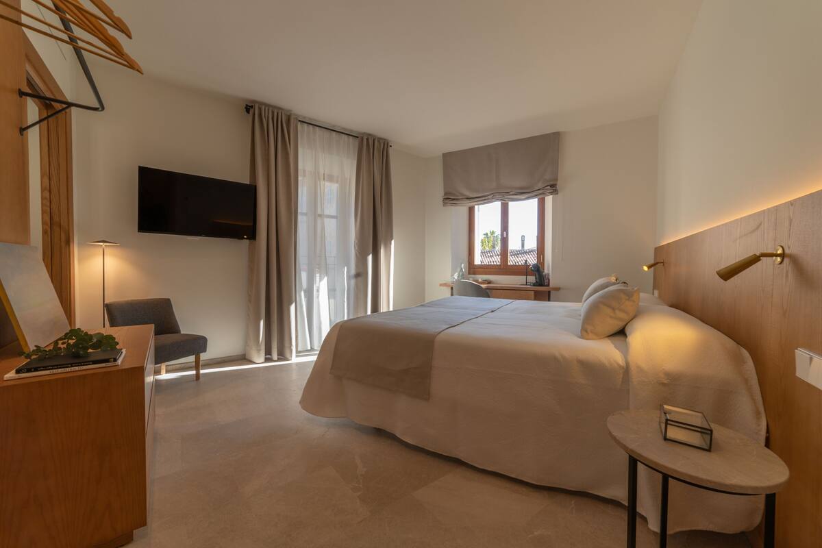 Een hotelkamer met een groot bed, een bureau met stoel, een aan de muur bevestigde televisie en een raam met gordijnen.