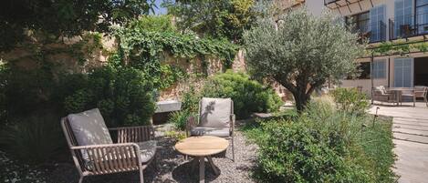 An outdoor seating area with wicker furniture, a round table, and a small garden with gravel and plants.