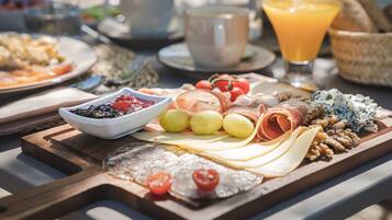 A breakfast spread with various cheeses, meats, and fruits on a wooden board.