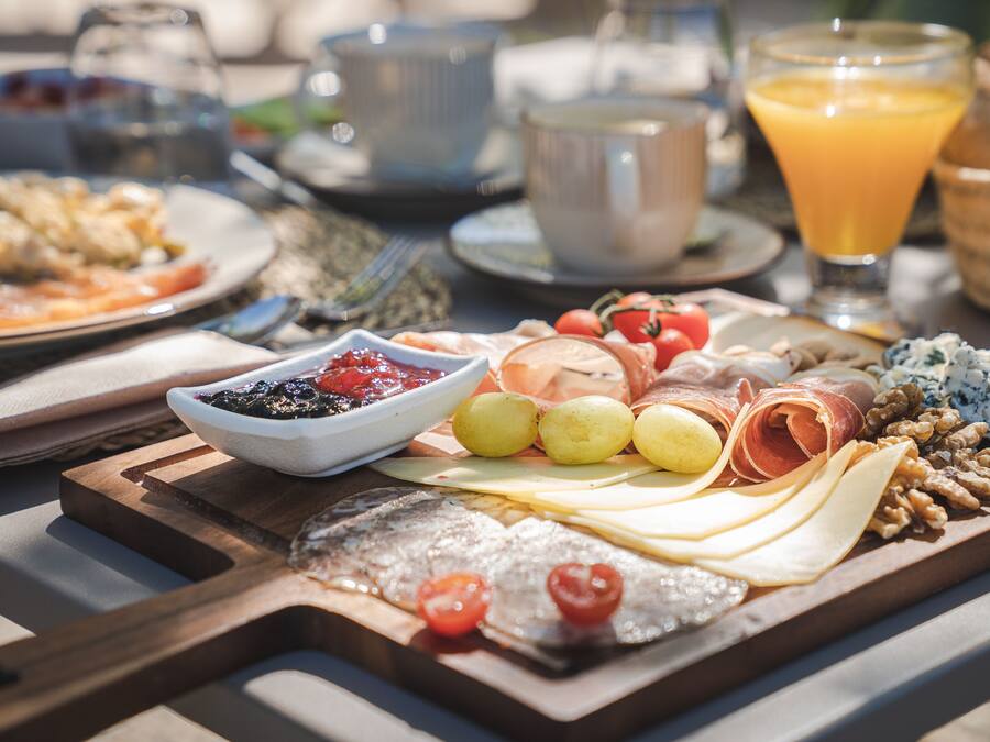 A breakfast spread with various cheeses, meats, and fruits on a wooden board.