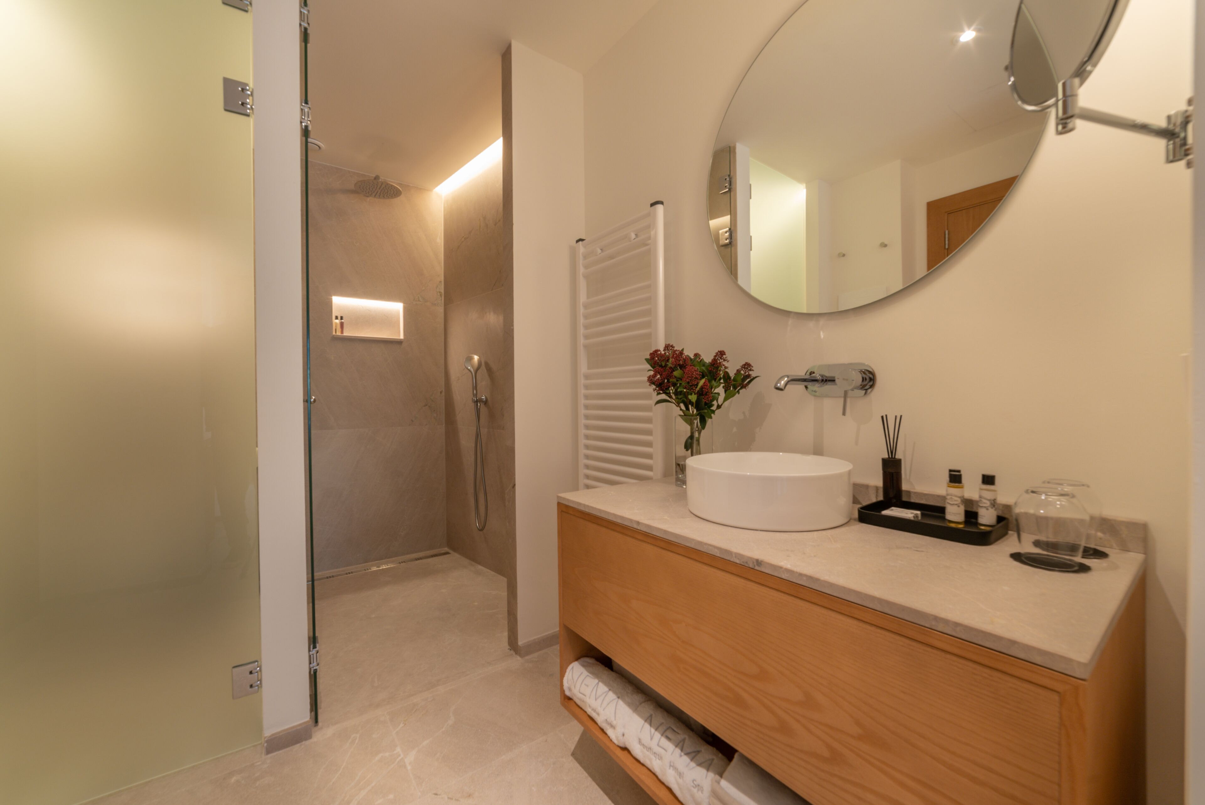 Une salle de bain moderne avec un miroir rond, un lavabo blanc et un meuble-lavabo en bois.