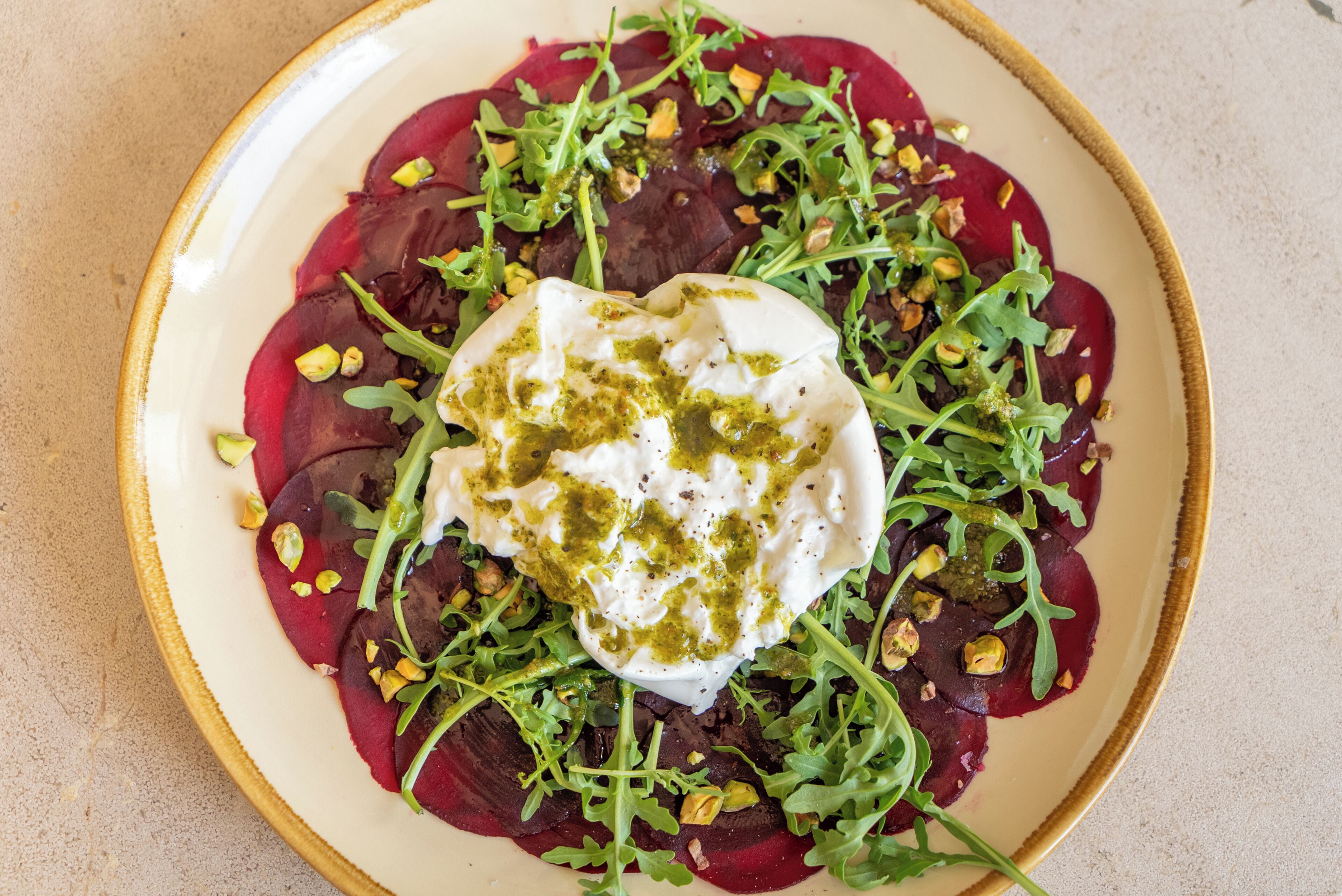 Une assiette de nourriture composée de betteraves, de légumes verts et d’une cuillère de crème.