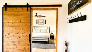 Una camera da letto con un letto, una ventola a soffitto, una insegna a parete e una porta in legno.