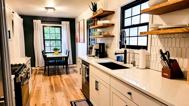 Una cucina moderna con zona pranzo, pavimento in legno e finestra con tende.