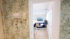 Un pasillo que conduce a una sala de estar con un sofá azul, una mesa de centro y un cuadro en la pared.