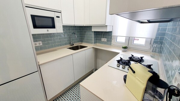 A compact kitchen with white cabinets, a built-in microwave, a gas stove, and a sink. - Retiro Park (Madrid)