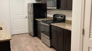 Compact kitchen area with a refrigerator, microwave, and oven, featuring a granite countertop and a light wood laminate floor.