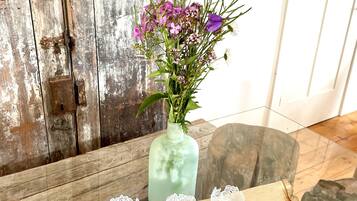 A rustic wooden door with a vintage metal lock, a glass table with a wooden base, and a vase with purple flowers and greenery.