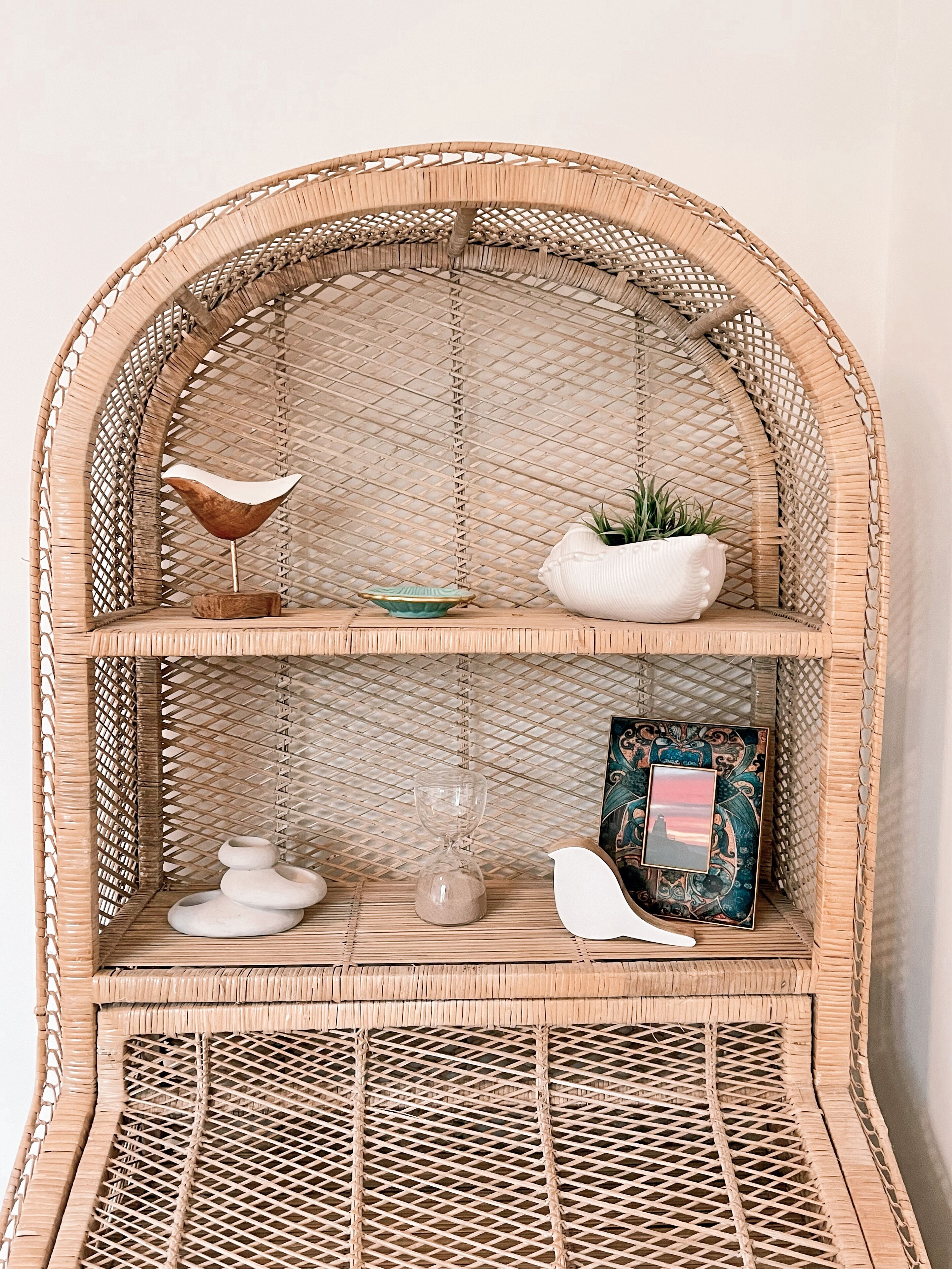 A wicker shelving unit with three shelves, each holding various decorative items.