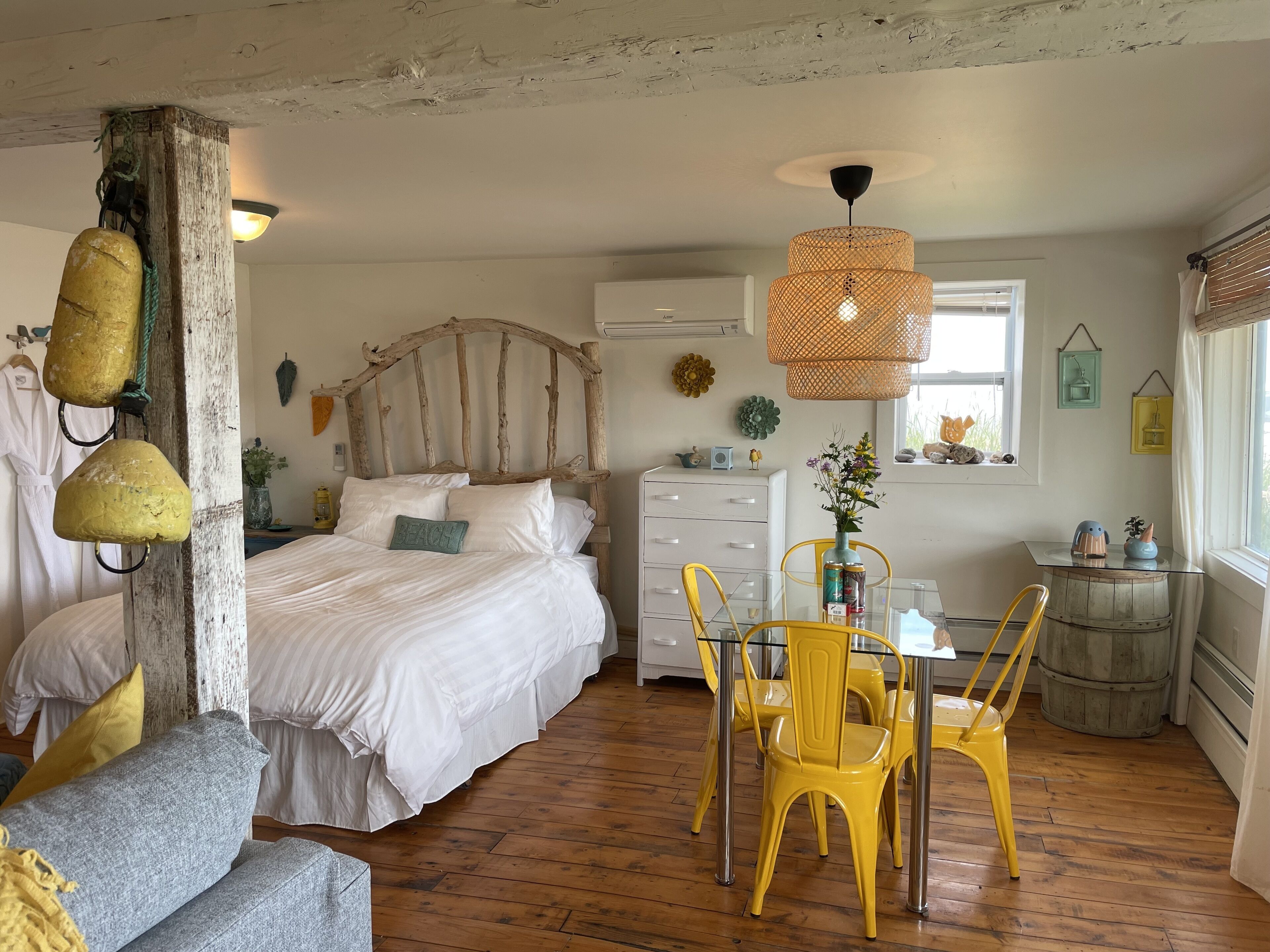 A bedroom with a wooden headboard, a bed with white linens, a small table with a vase, and a window with blinds.