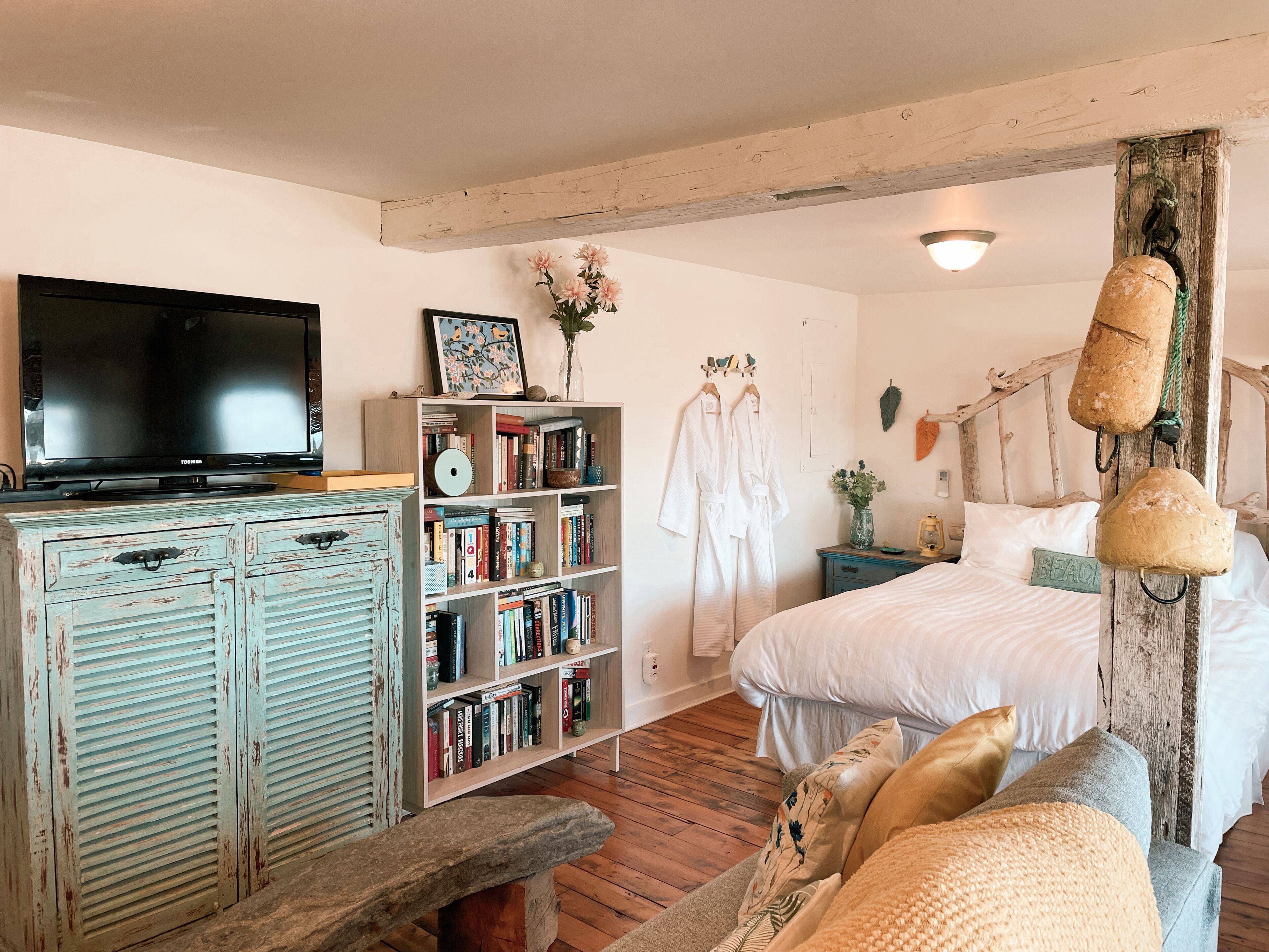 A bedroom with a bed, a TV, a bookshelf, and a wooden bench.