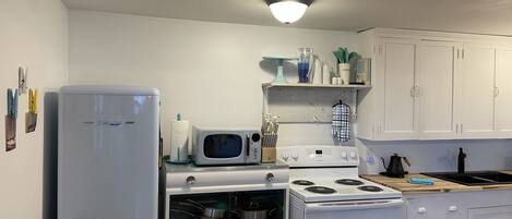 A kitchen with white appliances, including a refrigerator, microwave, and stove. There are cabinets and a shelf with various kitchen items.