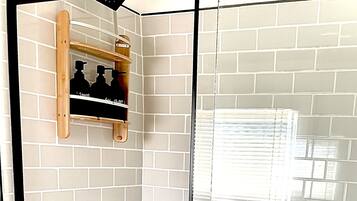A glass-enclosed shower with white tiled walls and a wooden shelf above.
